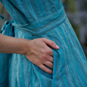 May include: A turquoise blue dress with thin white stripes. The dress has a tie at the waist and a pocket on the side.