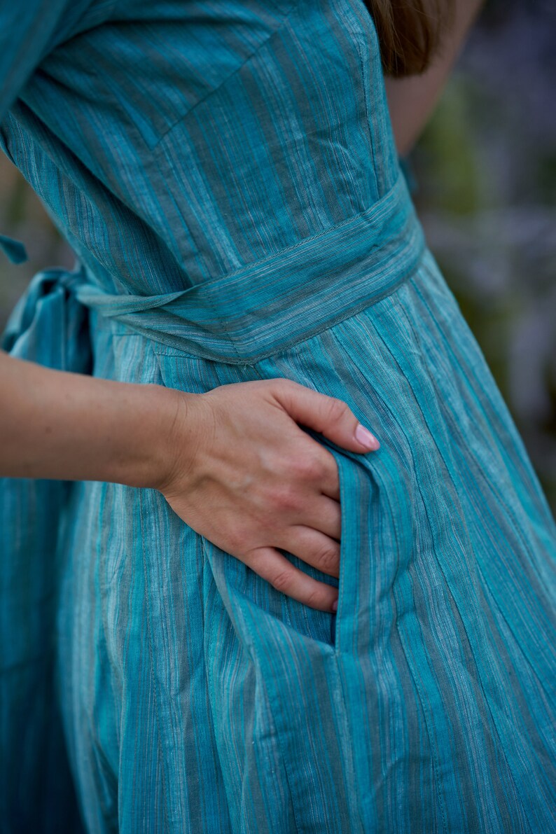 May include: A turquoise blue dress with thin white stripes. The dress has a tie at the waist and a pocket on the side.