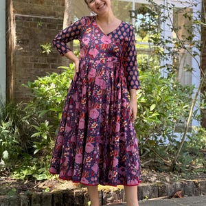 May include: A navy wrap dress with a floral print in pink and red. The dress has three-quarter sleeves and a V-neck. The dress is worn with brown sandals.