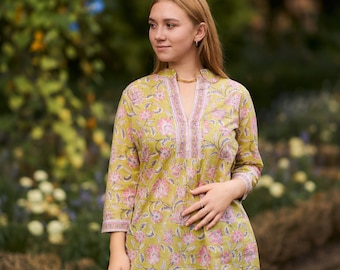 May include: A woman wearing a green and pink floral print tunic top with a V-neck and three-quarter sleeves. She is wearing blue jeans and a silver necklace.