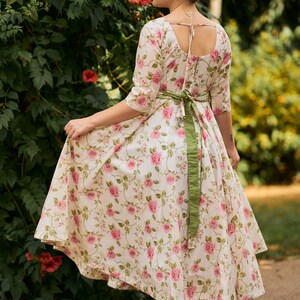 May include: A white dress with a floral print and a green sash. The dress has a scoop neckline and a flowy skirt.