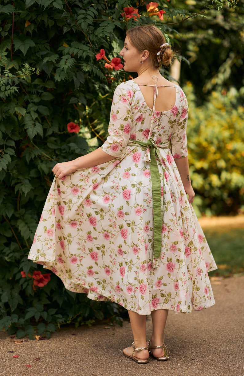May include: A white dress with a floral print and a green sash. The dress has a scoop neckline and a flowy skirt.