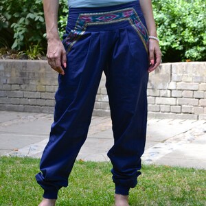 May include: A pair of navy blue pants with a colorful patterned waistband. The pants are cuffed at the bottom and the person is wearing them barefoot.