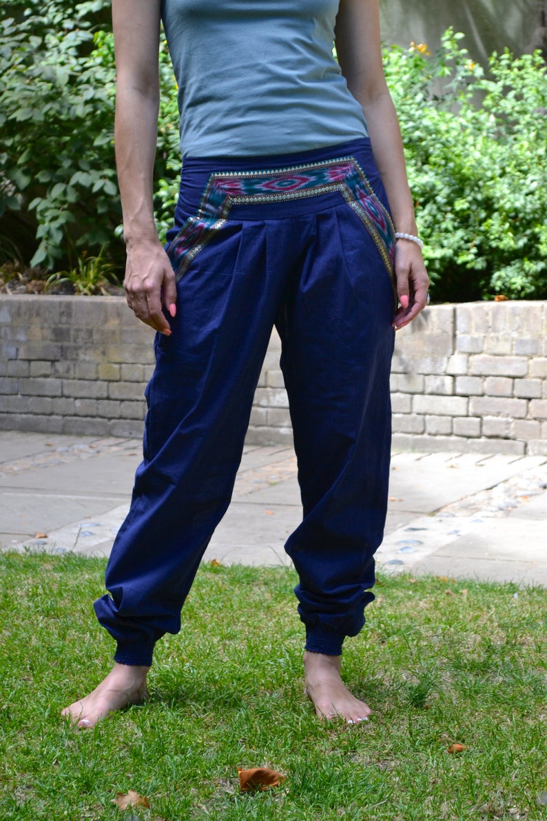 May include: A pair of navy blue pants with a colorful patterned waistband. The pants are cuffed at the bottom and the person is wearing them barefoot.