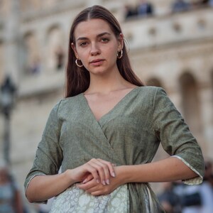 May include: A woman wearing a green linen wrap dress with a floral print underneath. The dress has a V-neckline and 3/4 sleeves.