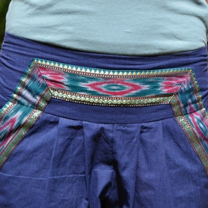 May include: Blue pants with a colorful patterned waistband. The waistband features a geometric design with red, green, and gold accents.