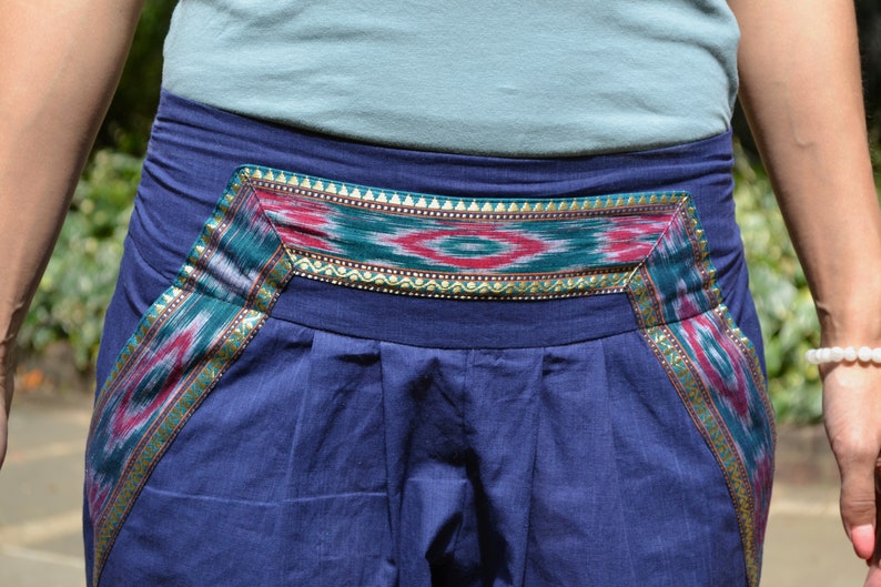 May include: Blue pants with a colorful patterned waistband. The waistband features a geometric design with red, green, and gold accents.