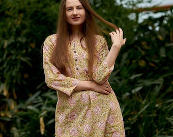 May include: A woman wearing a yellow and pink floral print tunic top with a button-up front and three-quarter sleeves. She is wearing blue jeans and has long brown hair.