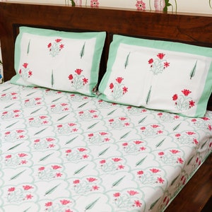 May include: A white bed with a green and pink floral patterned bedspread and two matching pillowcases. The bed has a wooden headboard.