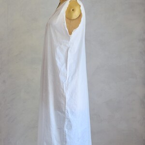 May include: A white sleeveless dress with a simple design, displayed on a dress form. The dress has a slightly gathered neckline and a straight, flowing silhouette.