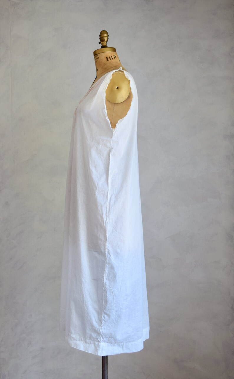 May include: A white sleeveless dress with a simple design, displayed on a dress form. The dress has a slightly gathered neckline and a straight, flowing silhouette.