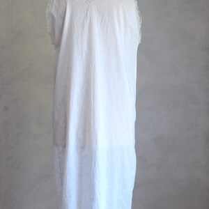 May include: A white sleeveless dress with a V-neckline and a pink trim around the neckline. The dress is on a white mannequin.