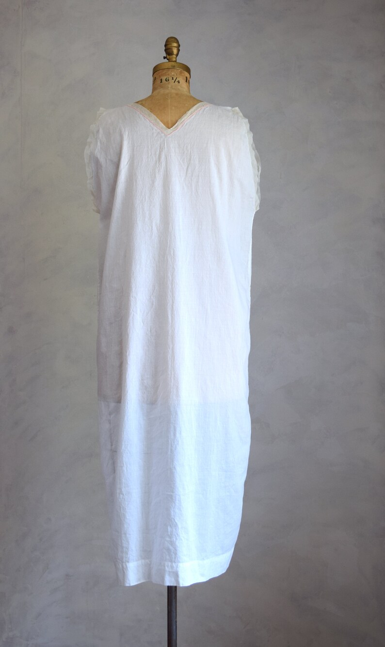 May include: A white sleeveless dress with a V-neckline and a pink trim around the neckline. The dress is on a white mannequin.