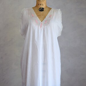 May include: A white cotton nightgown with pink embroidery around the neckline. The nightgown is sleeveless and has a V-neck.
