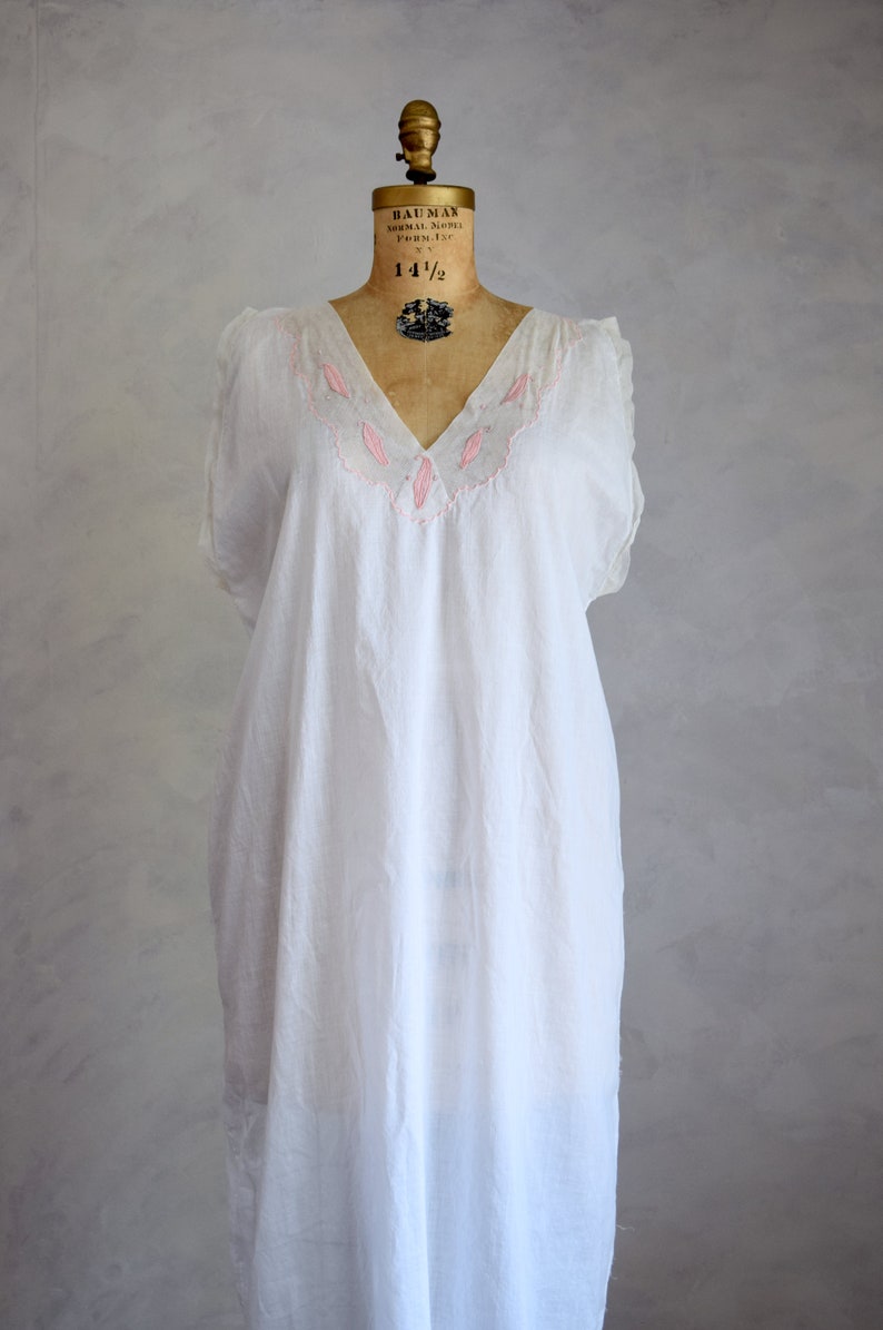May include: A white cotton nightgown with pink embroidery around the neckline. The nightgown is sleeveless and has a V-neck.