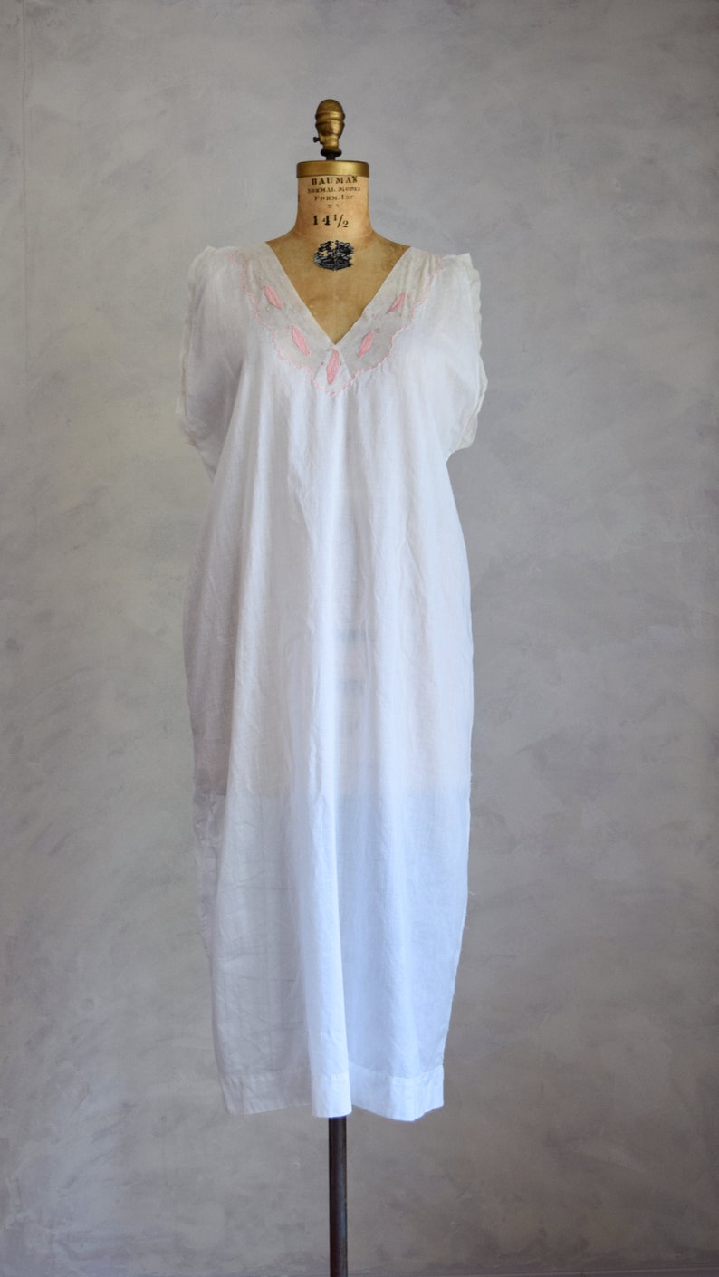 May include: A white cotton nightgown with pink embroidery around the neckline. The nightgown is on a dress form.