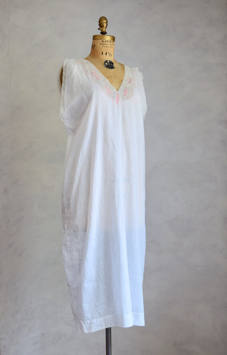 May include: A white cotton nightgown with pink embroidered leaves around the neckline. The nightgown is sleeveless and has a V-neck.