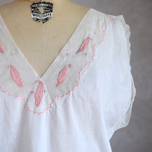 May include: White cotton sleeveless top with a pink embroidered neckline featuring a scalloped edge and leaf designs. The label reads "Wolf Form Co. N.Y.C."