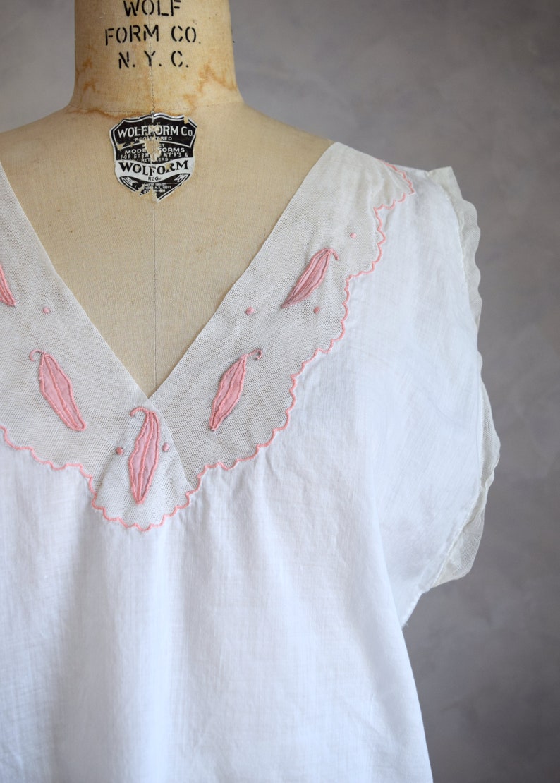 May include: White cotton sleeveless top with a pink embroidered neckline featuring a scalloped edge and leaf designs. The label reads "Wolf Form Co. N.Y.C."