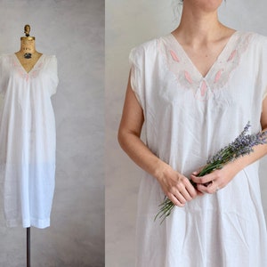 May include: A white cotton nightgown with a pink embroidered neckline. The nightgown has a sleeveless design and a loose fit.