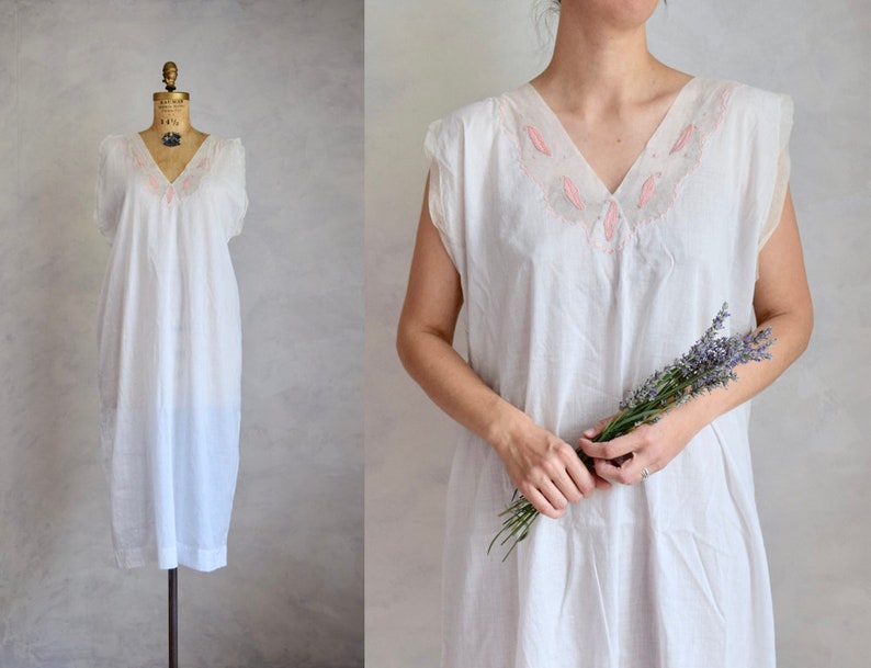 May include: A white cotton nightgown with a pink embroidered neckline. The nightgown has a sleeveless design and a loose fit.