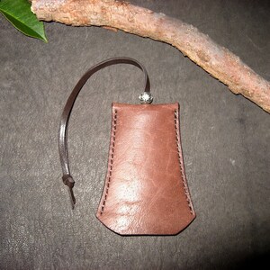May include: A brown leather pouch with a silver clasp and a brown leather strap. The pouch is on a brown surface.