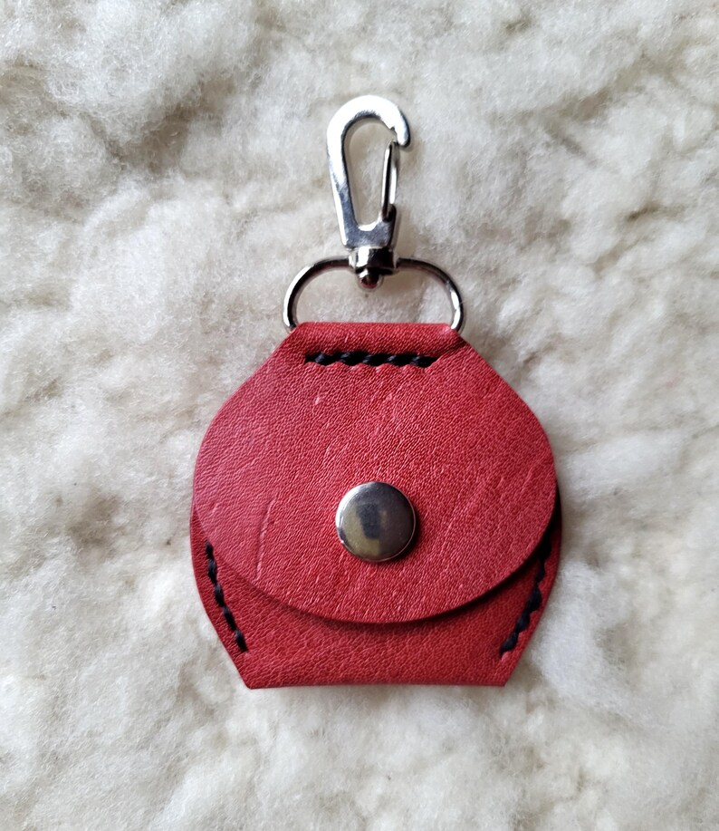 May include: A red leather keychain with a silver clasp and a silver button closure.