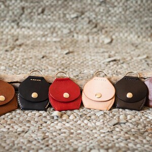 May include: Seven leather keychains in different colors, including brown, black, red, beige, and brown. Each keychain has a small flap with a gold button.