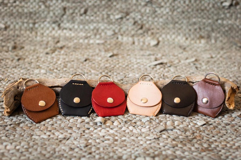May include: Seven leather keychains in different colors, including brown, black, red, beige, and brown. Each keychain has a small flap with a gold button.