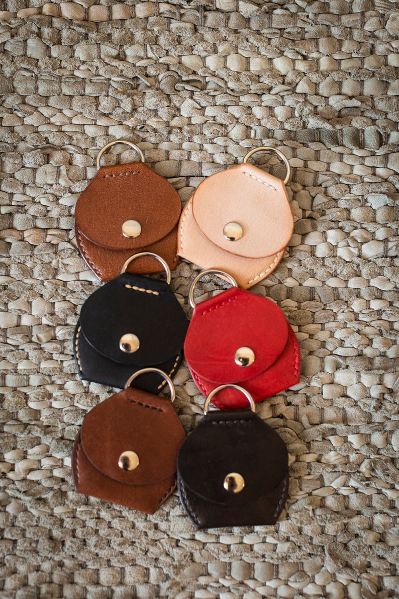 May include: Six leather keychains with a small pocket and a metal ring. The keychains are in different colors, including brown, black, red, and beige.