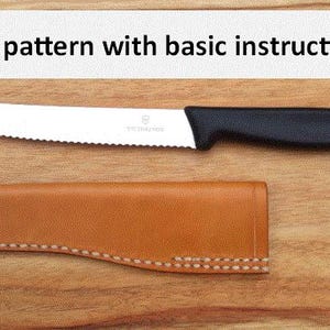 May include: A brown leather knife sheath with a stitched edge, laying on a wooden surface. A serrated knife with a black handle is laying next to the sheath. The text "DIY pattern with basic instructions" is at the top of the image.