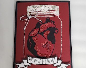 Tarjeta de felicitación gótica de San Valentín con corazón anatómico en un frasco.