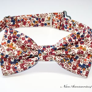 May include: A white bow tie with a floral pattern in shades of red, orange, blue, and brown. The bow tie has an adjustable strap.