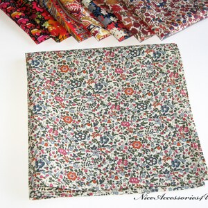 May include: A white cotton handkerchief with a small floral pattern in shades of pink, red, blue, and green. The handkerchief is folded in half and has a slightly frayed edge.