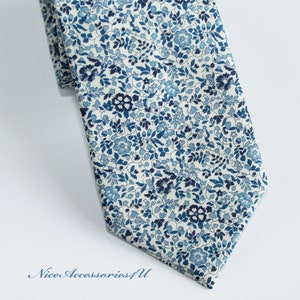 May include: A blue and white floral patterned necktie. The tie has a small, repeating pattern of blue flowers and leaves on a white background.