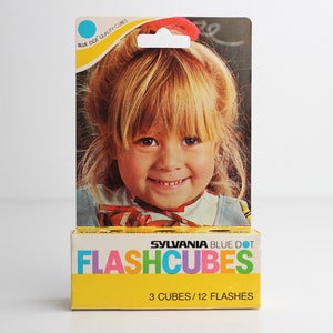 May include: A yellow box with the words "SYLVANIA BLUE DOT FLASHCUBES" in colorful letters. The box has a picture of a young girl with blonde hair smiling. The text on the box also says "3 CUBES/12 FLASHES".