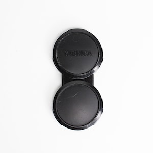 May include: A black camera lens cap with the word "YASHICA" printed on it.