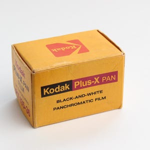 以下が含まれることがあります： ヴィンテージのKodak Plus-X PANフィルムの箱。箱はマスタードイエロー色で、Kodakのロゴは赤と黒です。箱のテキストは「Kodak Plus-X PAN BLACK-AND-WHITE PANCHROMATIC FILM」と書かれています。