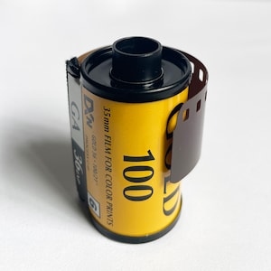 May include: A roll of 35mm film for color prints, labeled "DN GOLD 36-100/21", with a yellow and black label and a black and brown plastic canister.