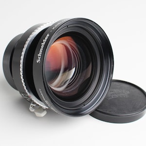 Op de afbeelding: Een zwarte Schneider Kreuznach lens met een zilveren ring en een zwarte lensdop. De lens heeft de tekst "Schneider - Kreuznach" op de zijkant.