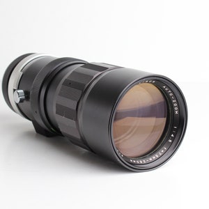 May include: A black camera lens with a silver ring and the text "AUTO ZOOM 1:4.5 135mm-250mm" printed on the side.