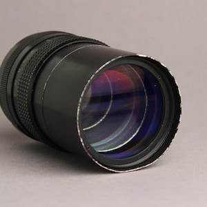 May include: A black camera lens with a silver ring around the front. The lens has a large, clear glass element with a purple and blue tint.