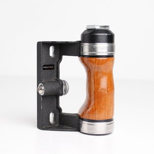 May include: A black and wood camera grip with a silver ring and the word "PENTAX" printed on the side.