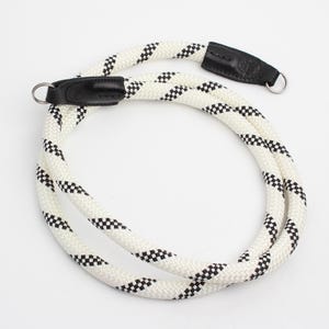 May include: A white and black checkered rope camera strap with black leather ends and silver metal rings. The strap is coiled and ready for use. The camera strap is a photography accessory.