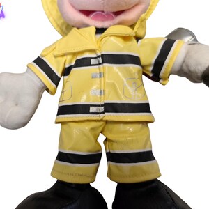 Puede incluir: Un peluche de un personaje con un uniforme de bombero amarillo con rayas negras. El juguete tiene guantes blancos y una cara sonriente. El uniforme incluye una chaqueta, pantalones y un casco.