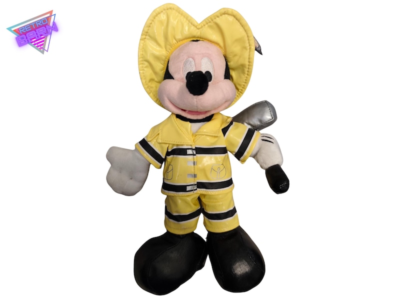 Puede incluir: Un peluche de Mickey Mouse vestido de bombero. El juguete lleva un casco, una chaqueta y un pantal&oacute;n de bombero amarillos con rayas negras. Tiene zapatos negros, guantes blancos y sostiene un hacha plateada. El juguete tiene una cara rosa y orejas negras.