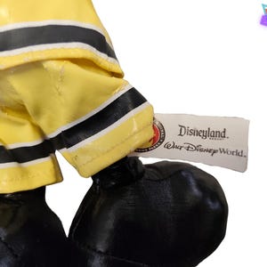 Puede incluir: Primer plano de un peluche con pantalones de bombero amarillos con rayas negras y zapatos negros. Una etiqueta dice "Disneyland Resort Walt Disney World."