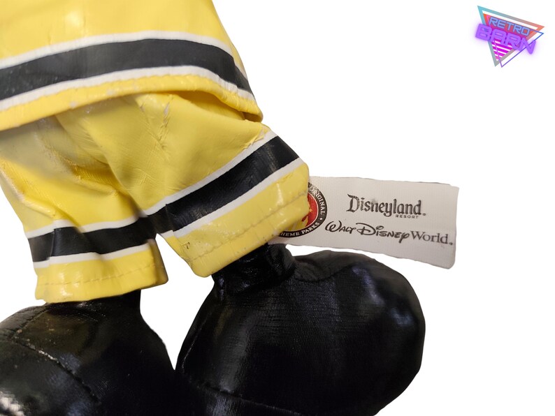 Puede incluir: Primer plano de un peluche con pantalones de bombero amarillos con rayas negras y zapatos negros. Una etiqueta dice "Disneyland Resort Walt Disney World."