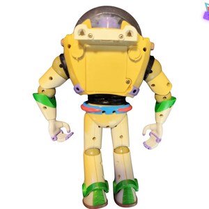 May include: A yellow and off-white Buzz Lightyear action figure with green and purple accents. The toy robot has a clear helmet and is standing with its arms at its sides. The Retro Geek logo is in the upper right corner.