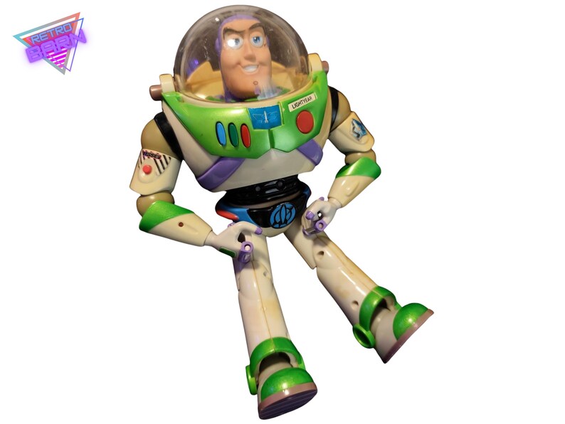 May include: A Buzz Lightyear action figure, featuring a clear helmet, green and white spacesuit, and a smiling face. The figure is in a seated position with its arms and legs extended. The figure has a "LIGHTYEAR" label on the helmet.